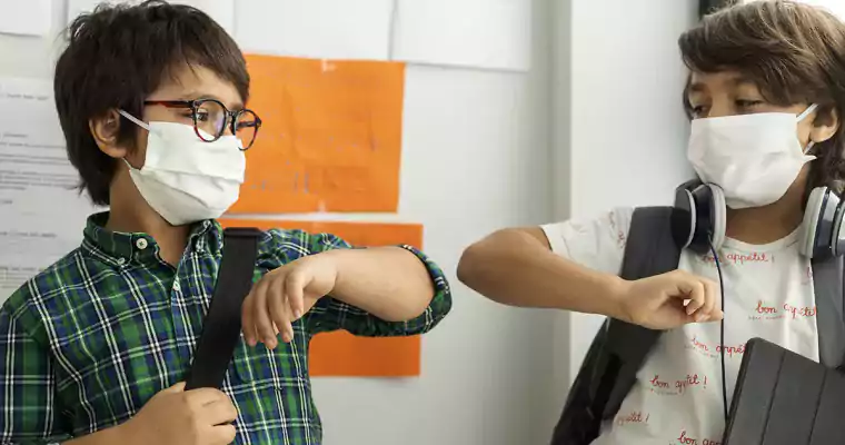 Two boys in masks with tablets elbow bumping